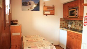 A compact kitchen with wooden cabinets, a microwave, and a small table with a patterned tablecloth. - Alpage Aga13 View & Mountain 3 Pers (Chatel)