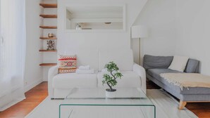 Ein modernes Wohnzimmer mit einem weißen Sofa, einem grauen Sofa, einem Glastisch und einer kleinen Topfpflanze.