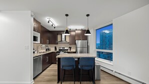 Una cocina moderna con una isla central, taburetes de bar, electrodomésticos de acero inoxidable, iluminación colgante y un amplio ventanal con vistas a la ciudad.