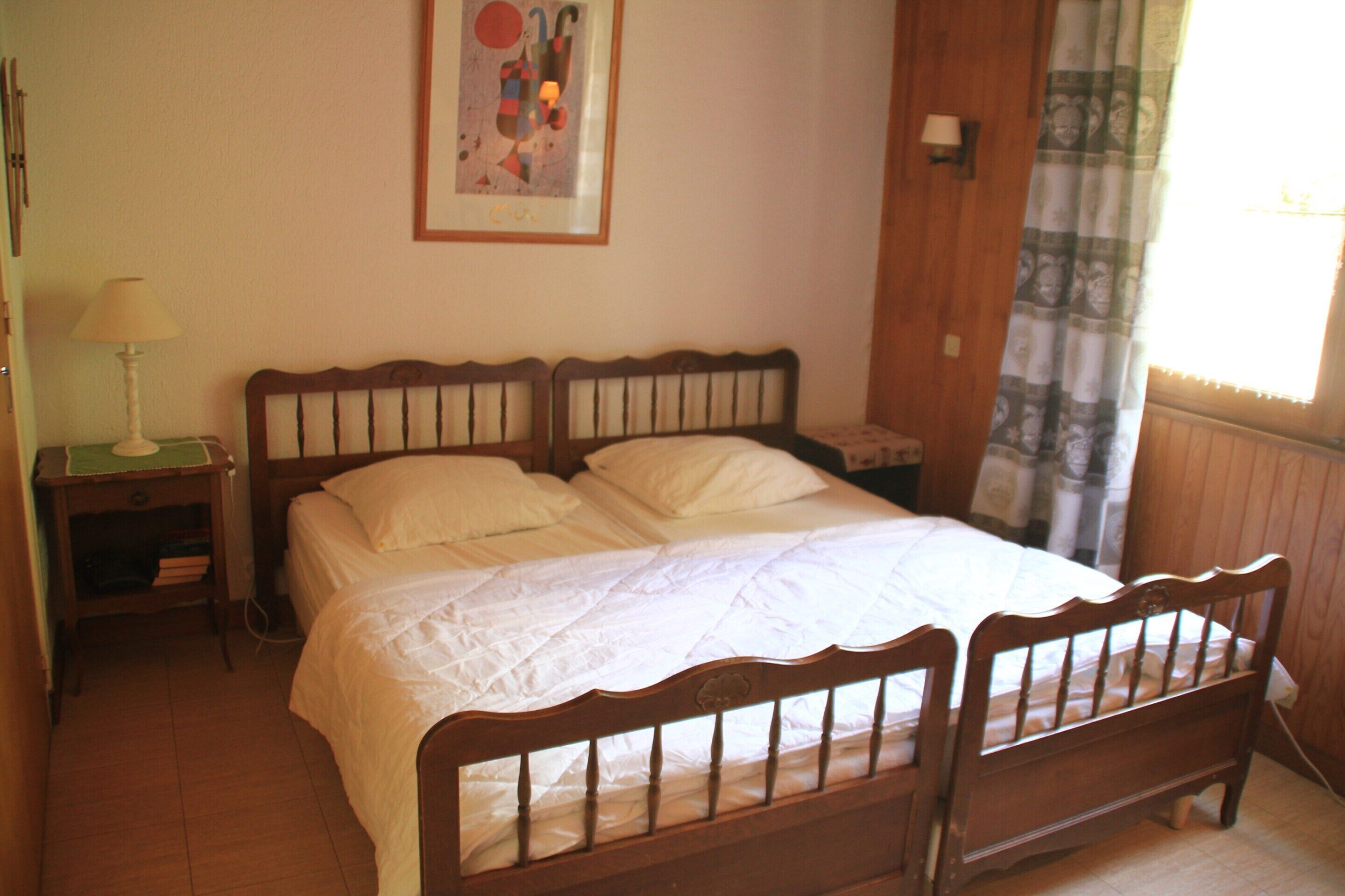 A bedroom with a wooden bed, white bedding, a nightstand with a lamp, and a painting on the wall.