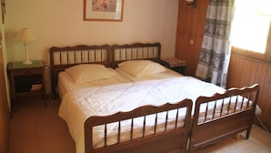Un dormitorio con cama de madera, ropa de cama blanca, una mesita de noche con lámpara y un cuadro en la pared.