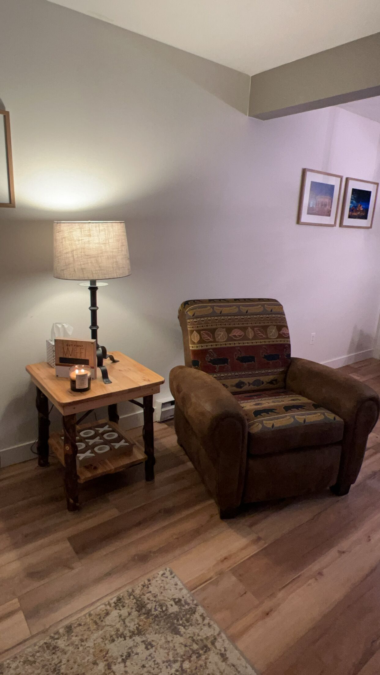A cozy living room with a wooden table, a lamp, a cushioned armchair, and a patterned rug.