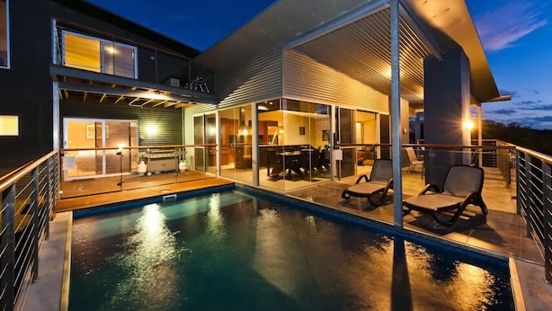 Una casa moderna con piscina, mobiliario exterior y un patio cubierto.