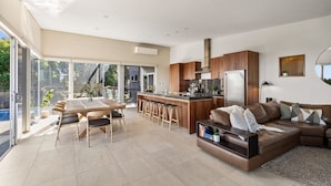 Una cocina moderna con una isla central, un comedor con mesa y sillas, y una sala de estar con sofá y televisor.