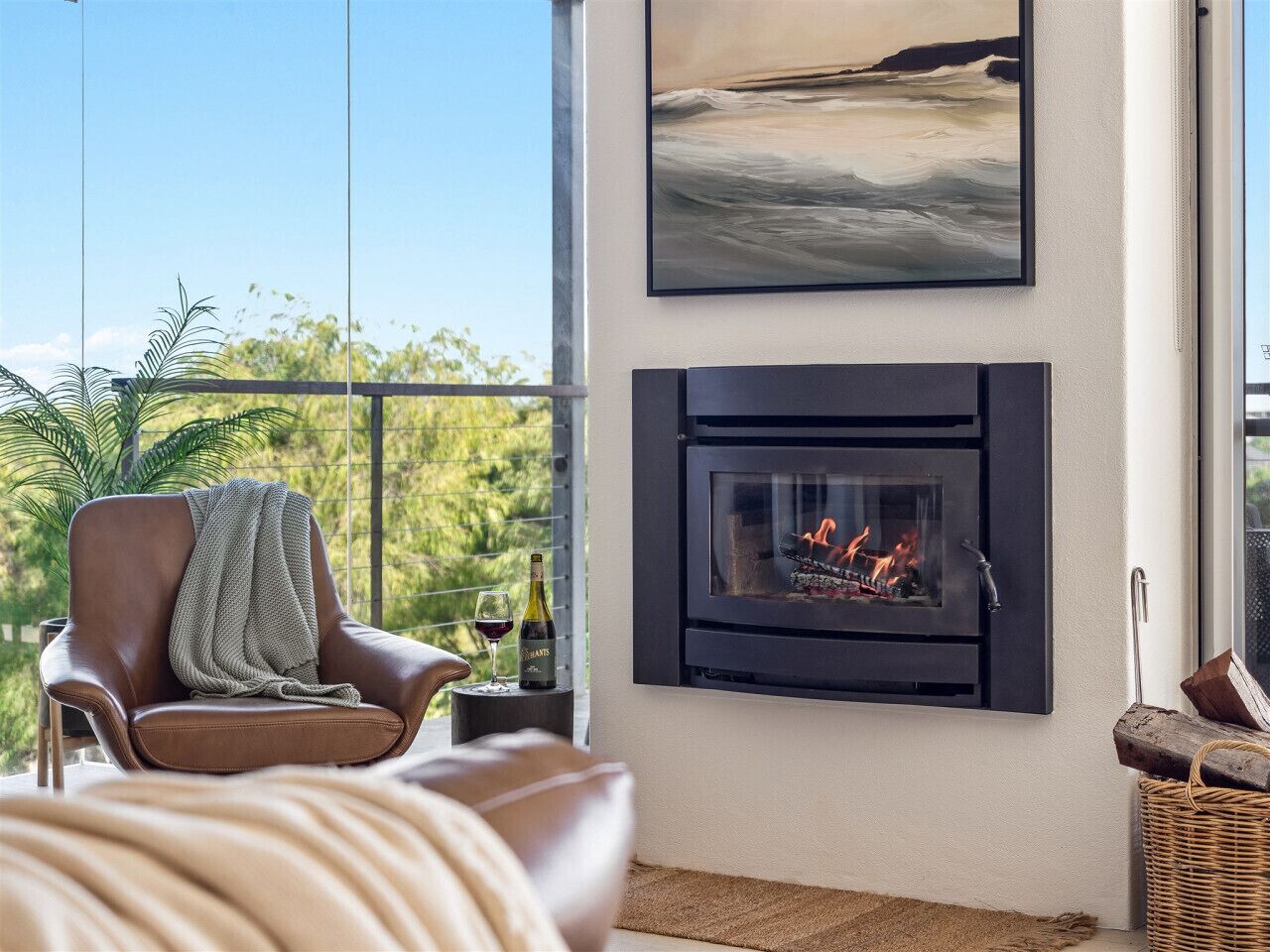 A modern living room with a fireplace, a comfortable leather chair, and a large window overlooking greenery.