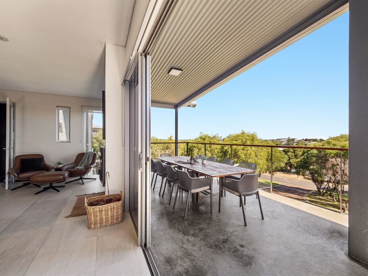 Een ruim balkon met een eettafel en stoelen, een rieten mand en uitzicht op het omliggende landschap.