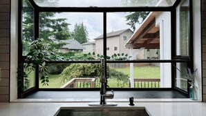 A kitchen with a large window, a stainless steel sink, and a view of a backyard and neighboring houses. - Spacious Modern Retreat w Game Room and Yard (Lynnwood)