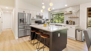 A modern kitchen with stainless steel appliances, a large island with stools, and pendant lighting. - Spacious Modern Retreat w Game Room and Yard (Lynnwood)