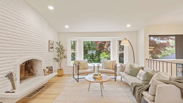 A living room with a white fireplace, two sofas, a coffee table, and a large window with a view of greenery. - Spacious Modern Retreat w Game Room and Yard (Lynnwood)