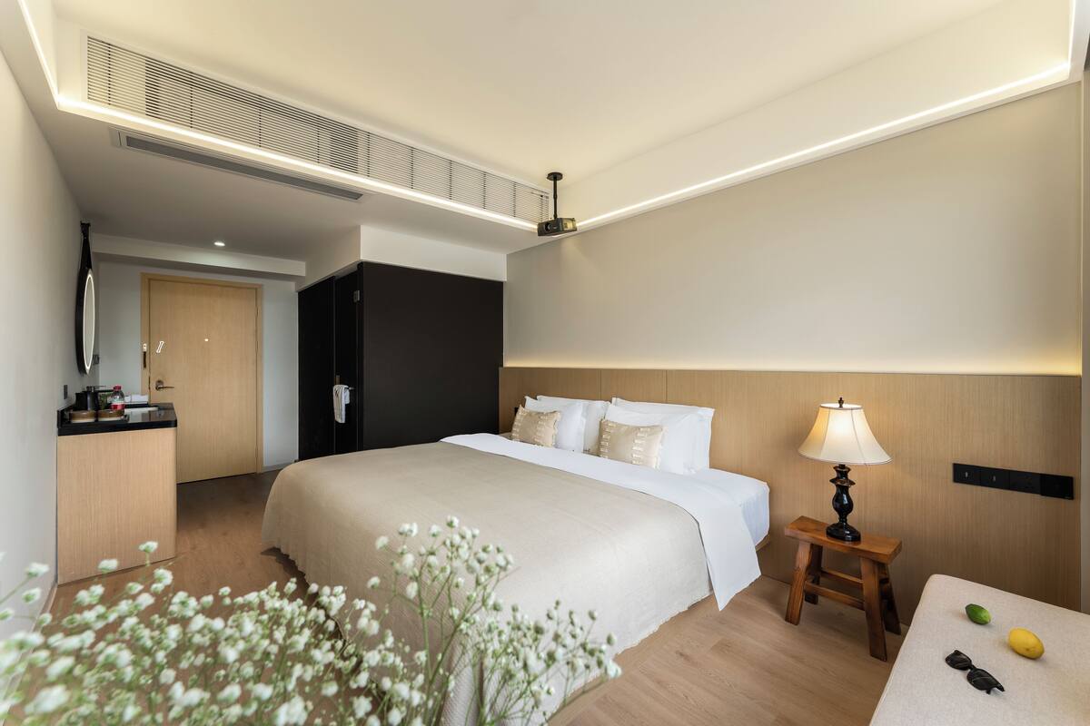 Hotellihuone, jossa on suuri sänky, yöpöytä, lamppu ja pieni pöytä, jossa on hedelmiä.