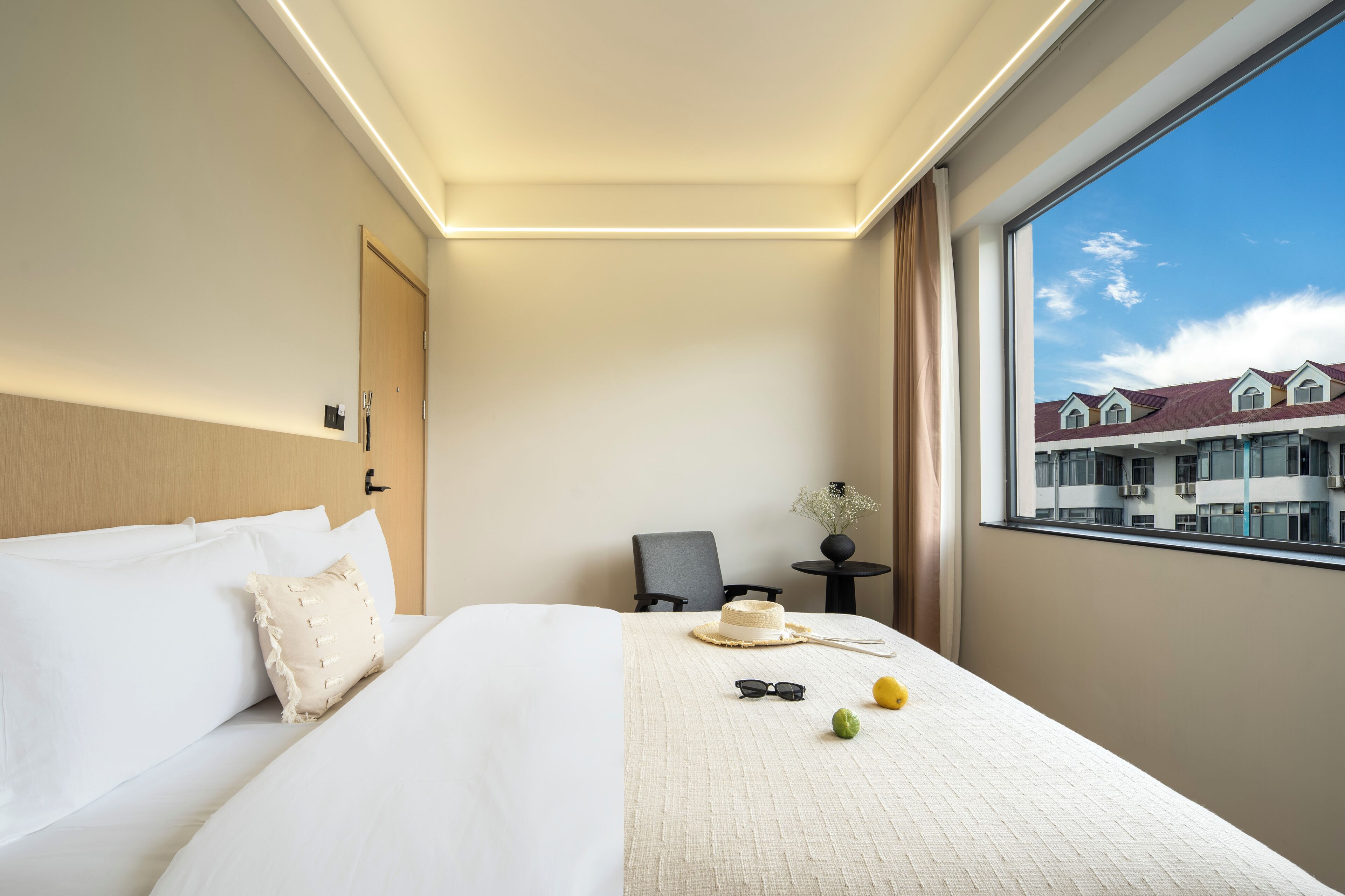 Habitación de hotel con una cama grande, una silla, una mesita y vistas a edificios a través del ventanal.
