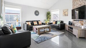 A modern living room with a black leather sofa, a wooden coffee table, and a stone accent wall. - Resort Experience: Pool, BBQ, Games with lots of space and fun in Pakenham (Pakenham)