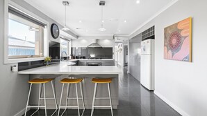 A modern kitchen with a large island, bar stools, and a view of the outdoors. - Resort Experience: Pool, BBQ, Games with lots of space and fun in Pakenham (Pakenham)