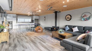 A modern living room with a sofa, coffee table, and a fireplace. There is a dining area with a table and chairs in the background. - Resort Experience: Pool, BBQ, Games with lots of space and fun in Pakenham (Pakenham)