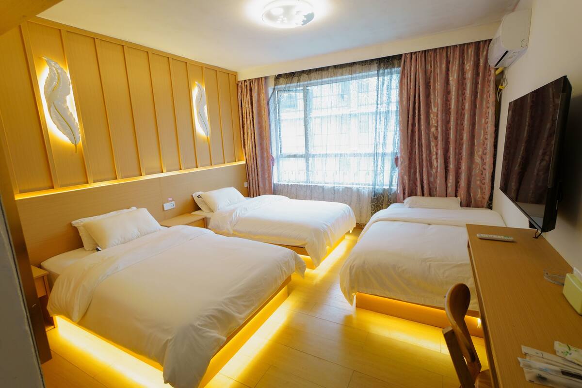 Een hotelkamer met drie bedden, een houten bureau en een televisie.