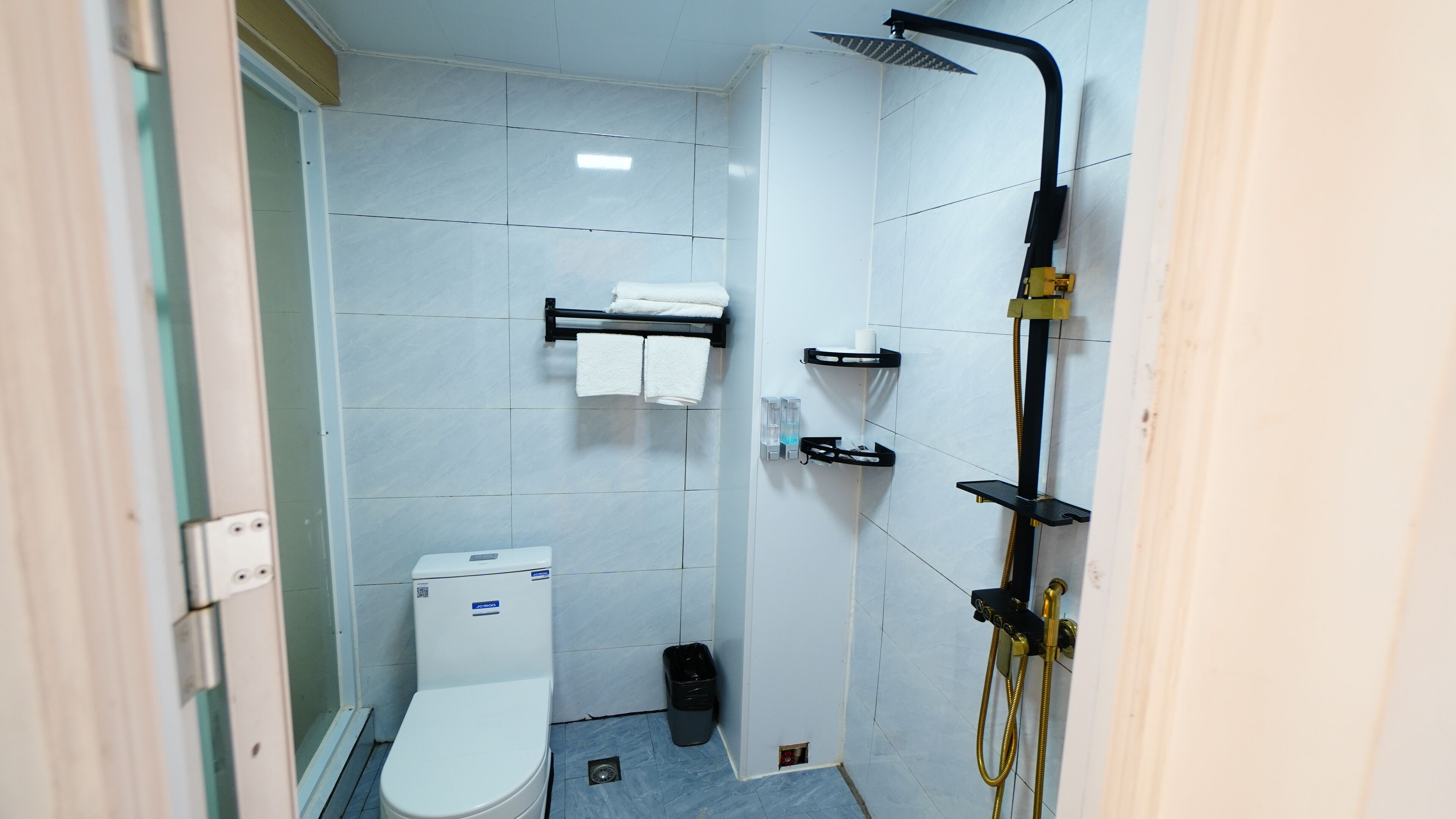 Ein kleines, sauberes Badezimmer mit Toilette, Handtuchhalter, Dusche mit Duschbrause und Mülleimer.