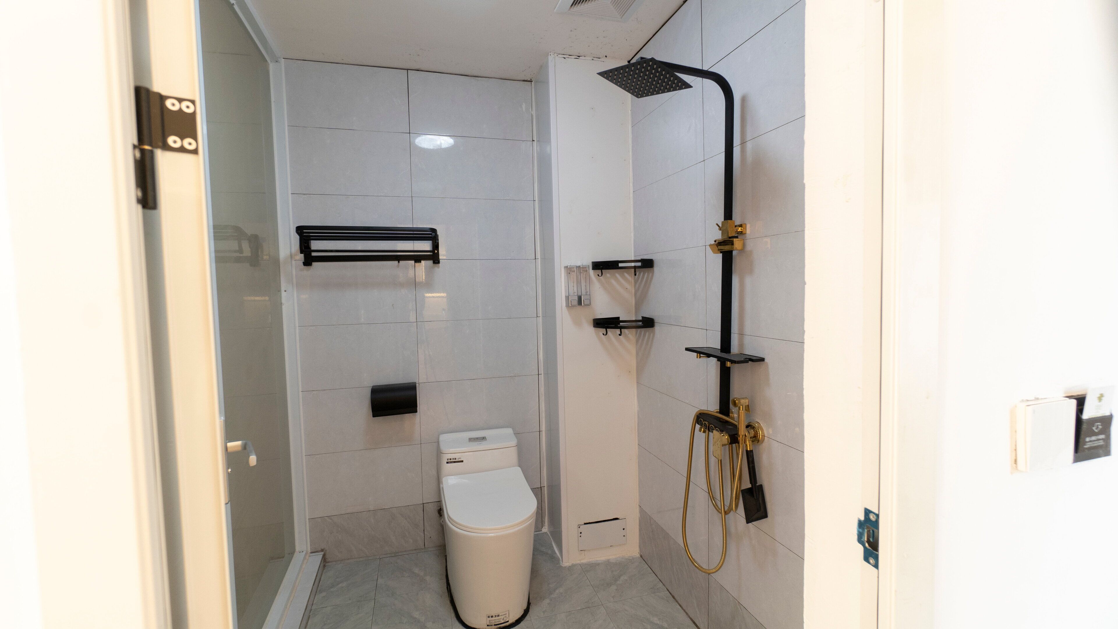 A modern bathroom with a toilet, a shower with a handheld showerhead, and a towel rack.
