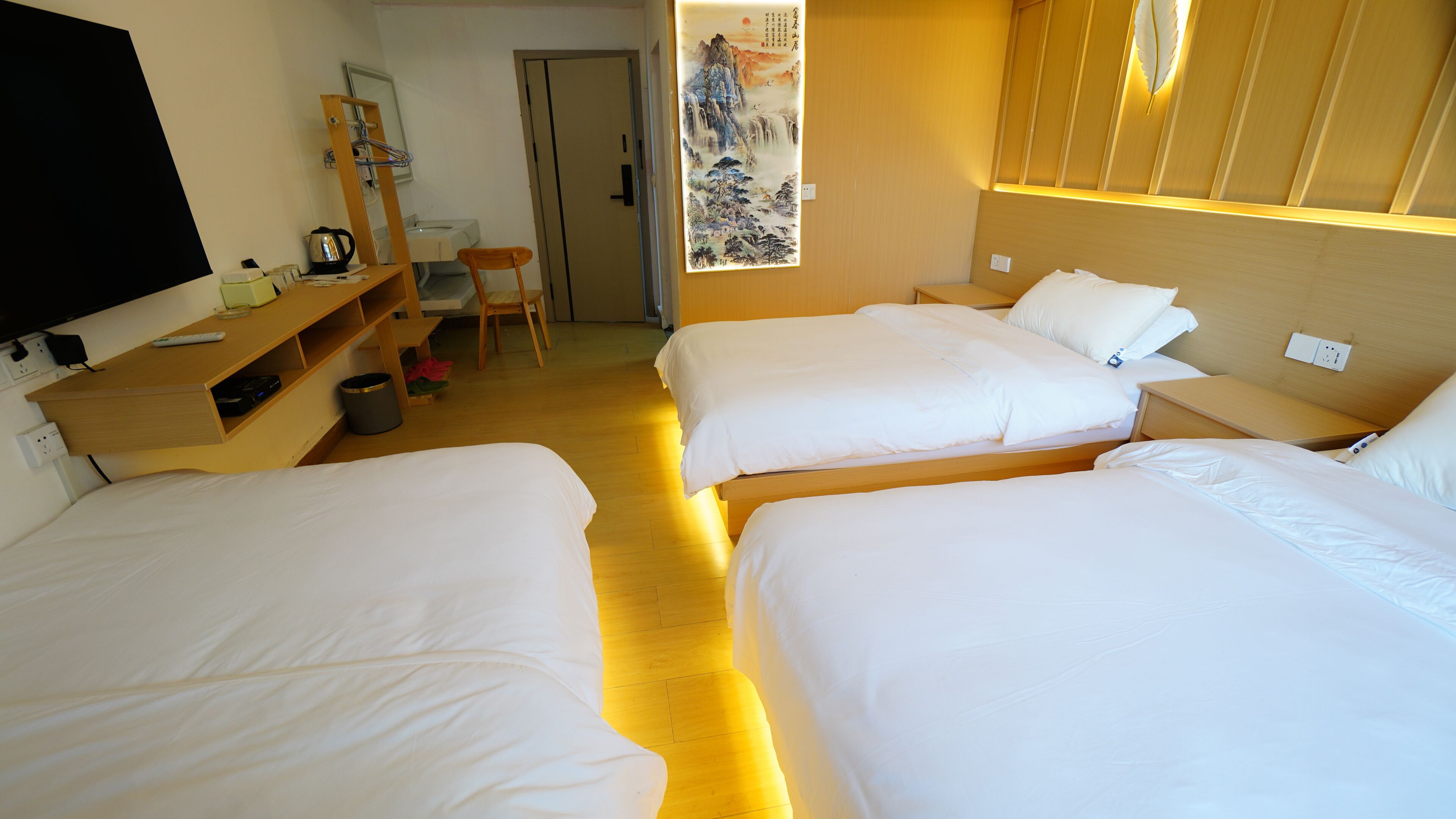 Une chambre d’hôtel avec trois lits, un bureau avec une chaise, une télévision et une œuvre d’art accrochée au mur.
