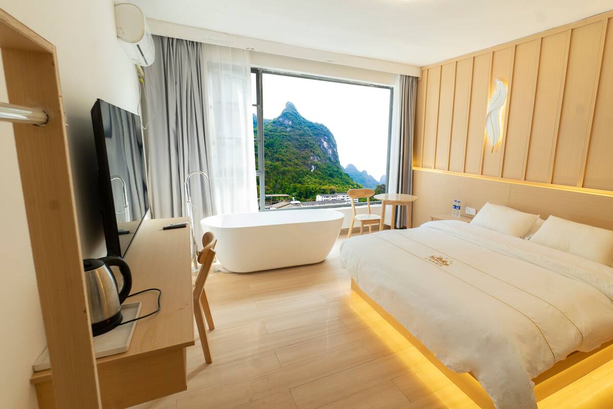 Een moderne hotelkamer met een groot bed, een badkuip, een bureau en uitzicht op een berg.