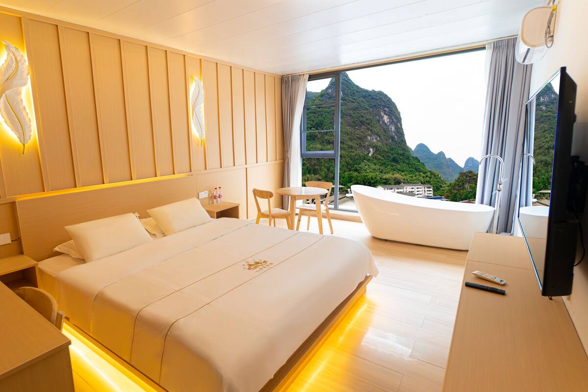 Een moderne hotelkamer met een groot bed, een tafeltje, een stoel en uitzicht op bergen door het raam.