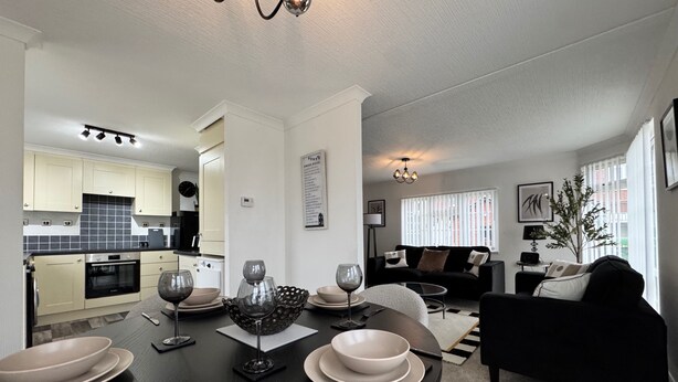 A modern kitchen with white cabinets, a dining area with a round table set for four, and a living room with a black sofa and a plant. - Paddock View - Snetterton, Norfolk (norwich)
