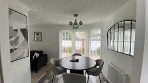 A dining area with a round table, four chairs, a chandelier, and large windows with a view of the outside. - Paddock View - Snetterton, Norfolk (norwich)