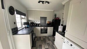 A compact kitchen with white cabinets, a black countertop, a washing machine, and a small refrigerator. - Paddock View - Snetterton, Norfolk (norwich)
