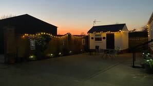 A courtyard with a small building, string lights, and a stone wall. - Paddock View - Snetterton, Norfolk (norwich)