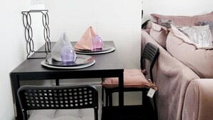 Ein ordentlich eingerichteter Raum mit einem schwarzen Metallstuhl, einem kleinen Tisch mit dekorativem Metallgestell und einem Bett mit rosa Decke.