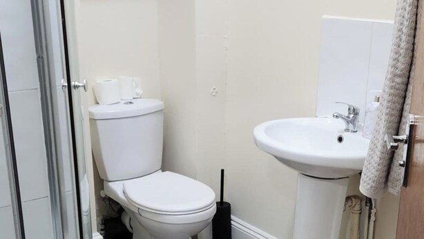 Une petite salle de bain propre, avec des toilettes, un lavabo et une serviette accrochée à la porte.