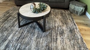 A living room with a grey sofa, two side tables with lamps, a round coffee table with decorative items, and a large window with curtains. - Cozy, 1-bedroom apartment with a pulled-out couch, close to all the facilities. (Porterville)