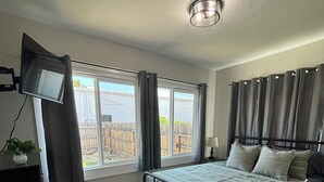 A bedroom with a bed, a TV mounted on the wall, and a window with curtains. - Cozy, 1-bedroom apartment with a pulled-out couch, close to all the facilities. (Porterville)