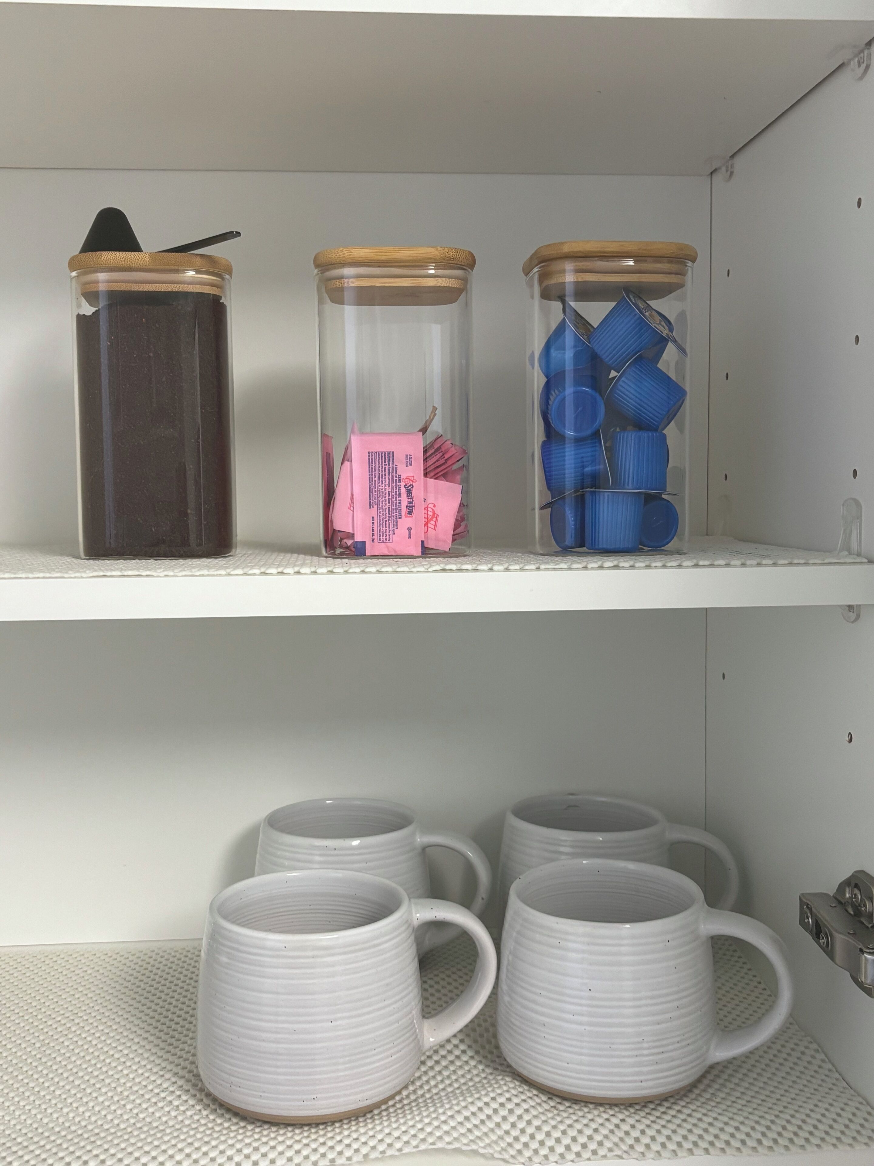 A shelf with three glass jars containing different items, and below it, three white mugs.