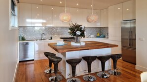 Une cuisine moderne dotée d’un îlot central, de tabourets de bar, d’appareils électroménagers en acier inoxydable et de luminaires suspendus.