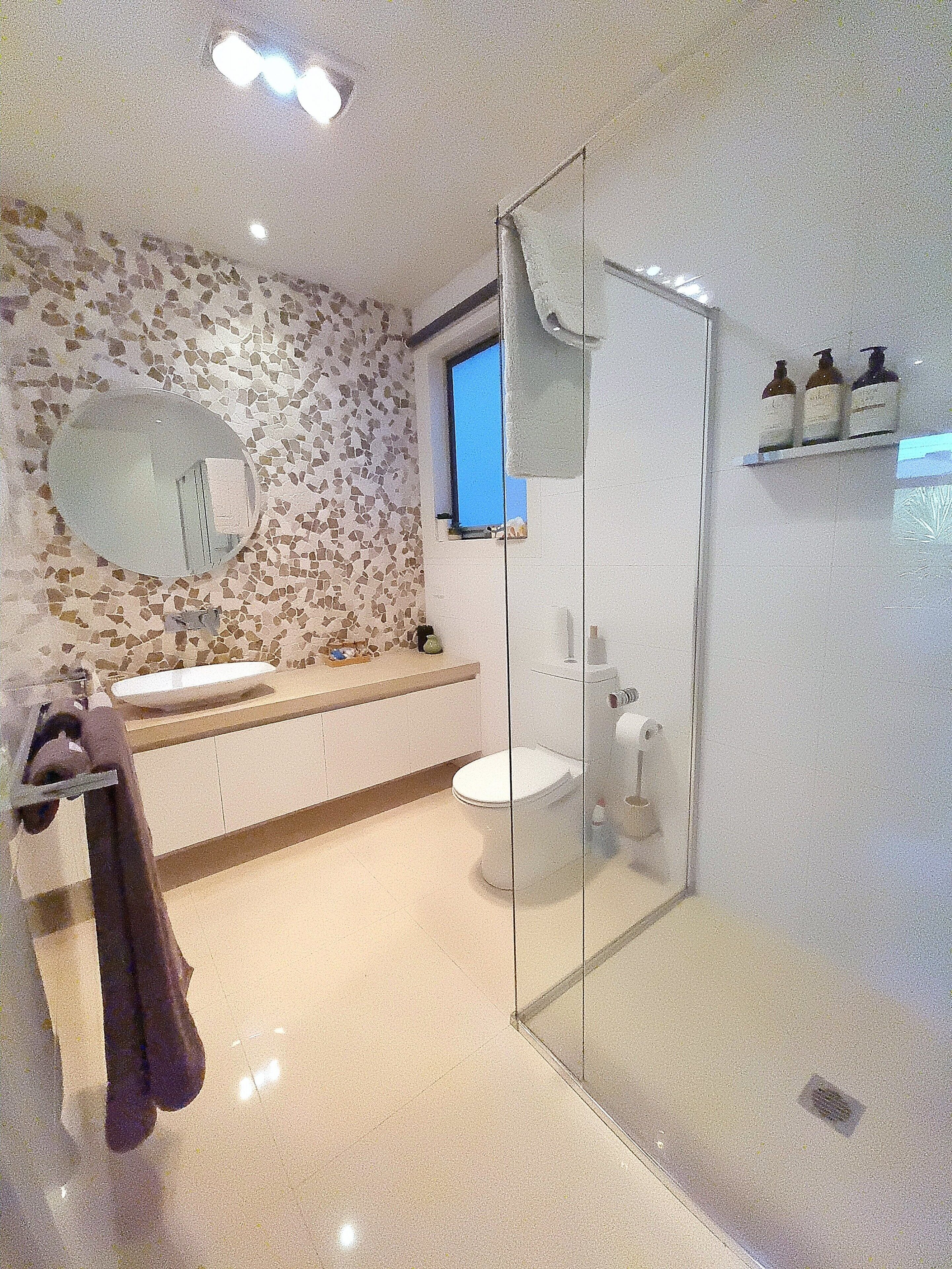 Ein modernes Badezimmer mit einer Mosaikwand, einem runden Spiegel, einer Duschkabine und einer Toilette.