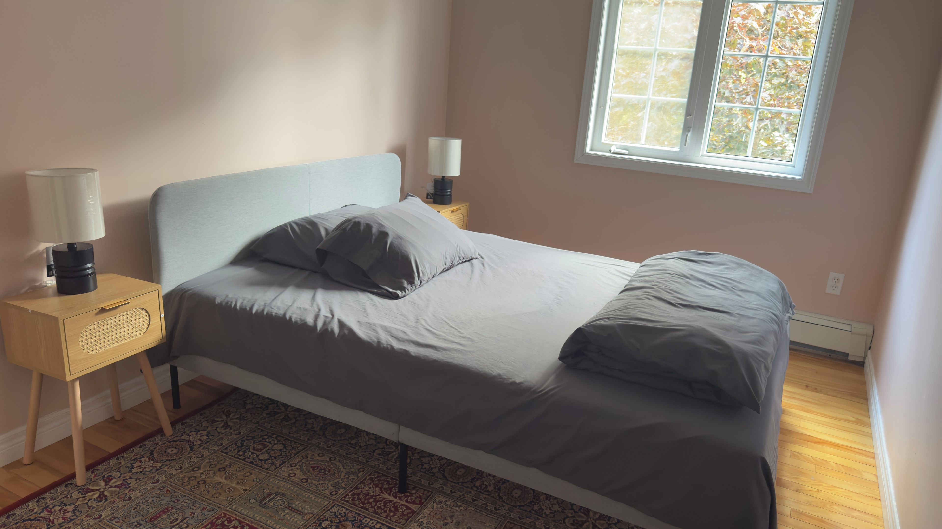 Ein Schlafzimmer mit Bett, Nachttisch, Lampe und Fenster.
