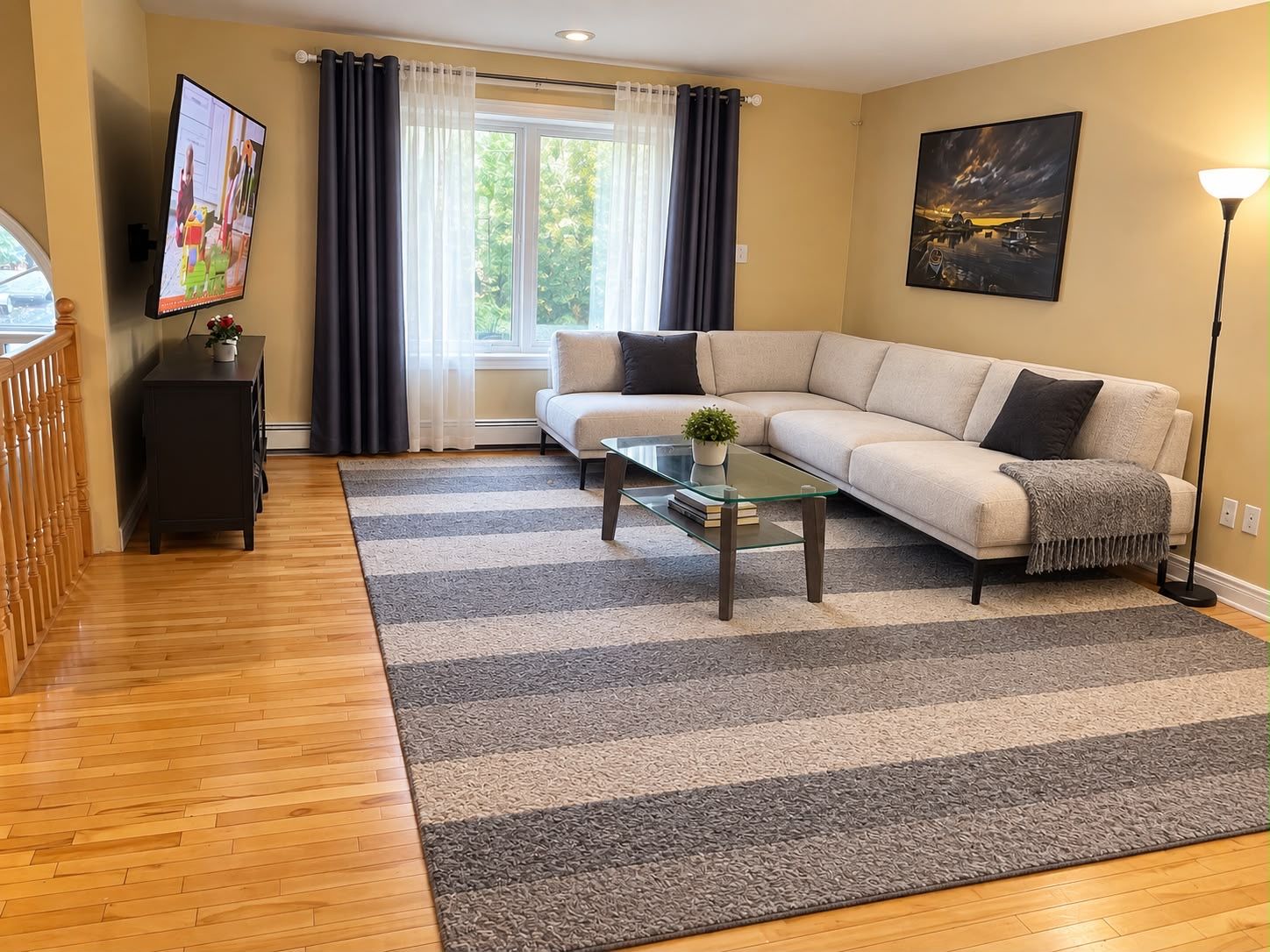En stue med sofa, sofabord, fjernsyn og et billede på væggen.