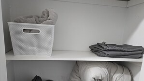 Vaatekaappi, jossa on hyllyjä, joilla säilytetään viikattuja vaatteita, sekä pyykkikori ja säilytyslaatikko.