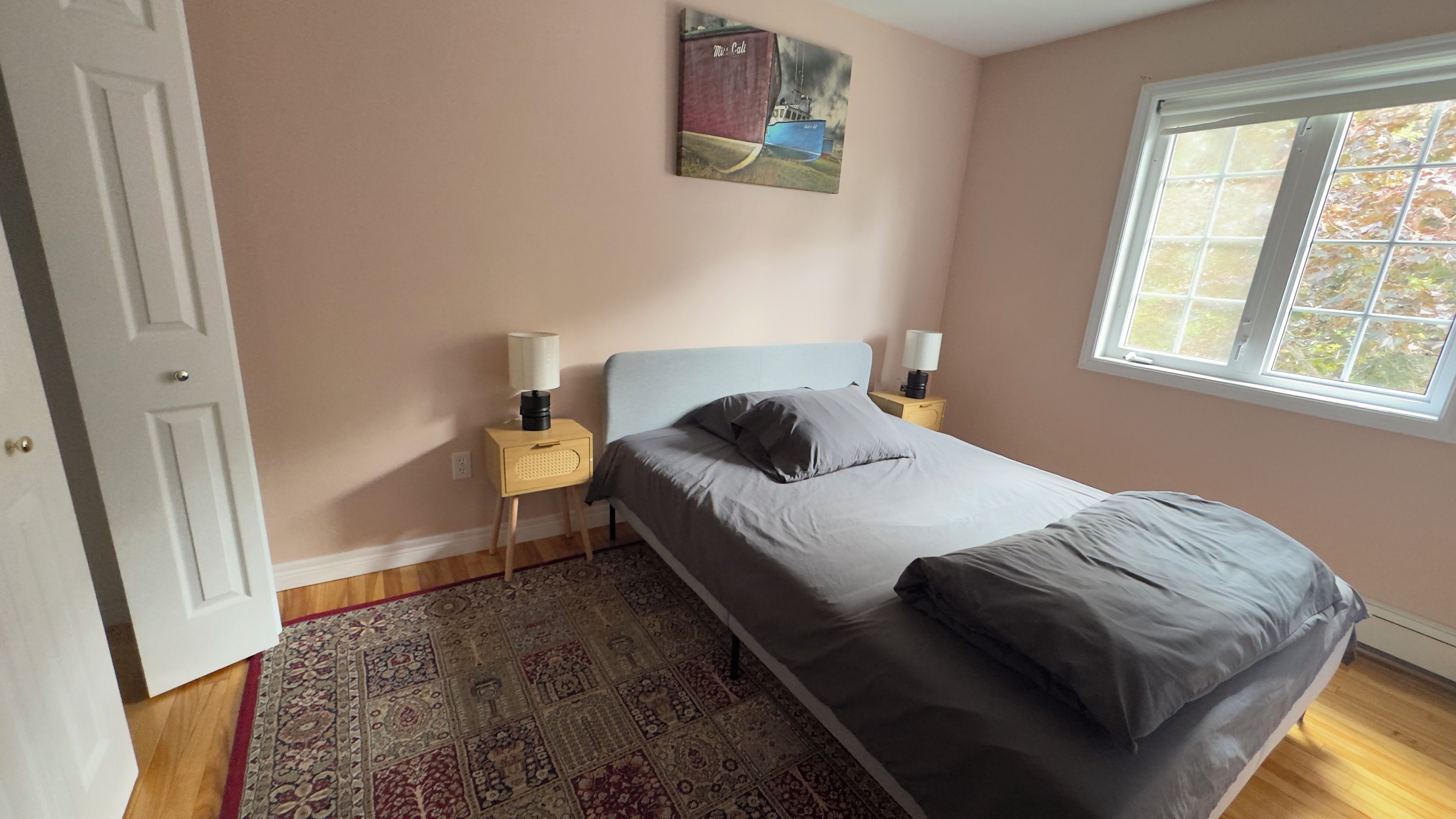 Un dormitorio con una cama, una mesita de noche, una lámpara, una alfombra y una ventana.