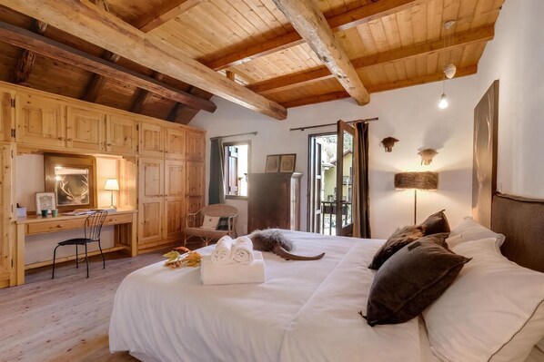 A cozy room with a large bed, wooden ceiling beams, a desk, and a chair.
