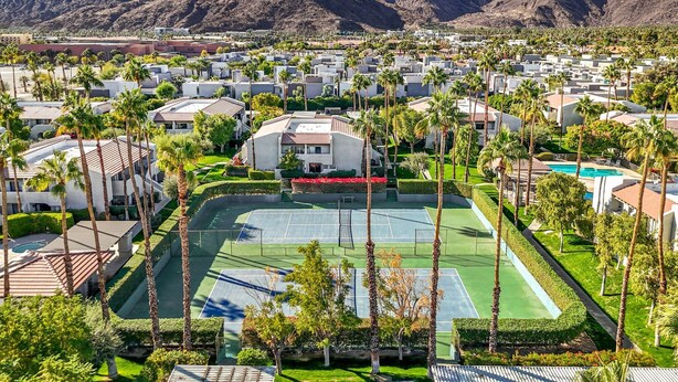 A residential area with modern houses, a tennis court, and a pool, surrounded by mountains.