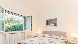 Een slaapkamer met een bed, een raam, een radiator, een nachtkastje met een lamp en een schilderij aan de muur.