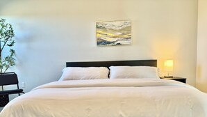 A neatly made bed with white linens, a dark headboard, and a wall-mounted abstract painting.