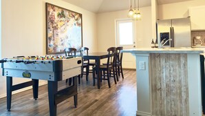 A modern kitchen with a central island, wooden flooring, and a dining area with a foosball table.