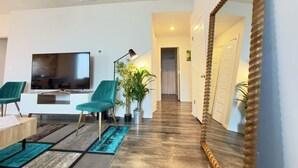 A modern living room with a flat-screen TV, teal chairs, a coffee table, and a large mirror.
