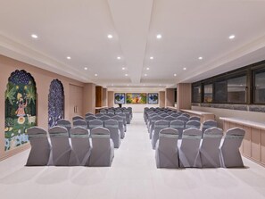 A conference room with rows of chairs, a stage, and artwork on the walls. - Regenta Dwarka (Dwarka)
