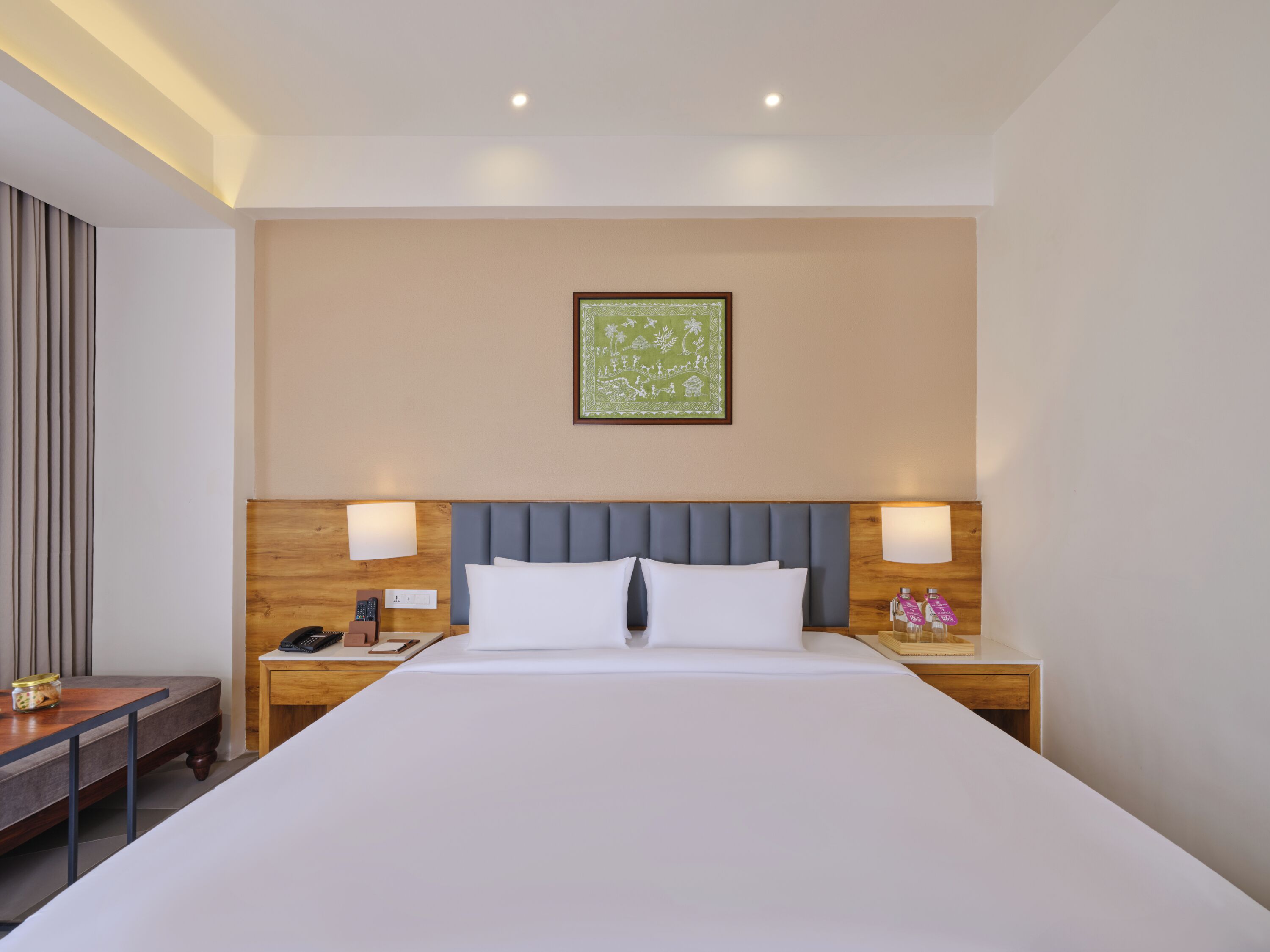 A hotel room with a large bed, two bedside tables, a nightstand, a desk, and a framed picture on the wall.