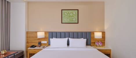 A hotel room with a large bed, two bedside tables, a nightstand, a desk, and a framed picture on the wall.
