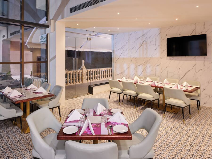 Un restaurante con paredes de mármol, varias mesas de comedor con sillas blancas, y un televisor grande colgado en la pared.