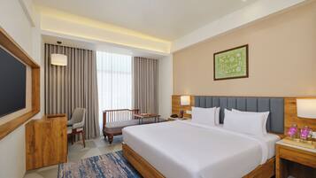 A hotel room with a large bed, a desk, a chair, a small table, and a window with curtains.